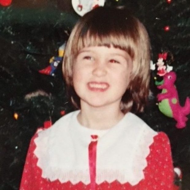 Young girl with bangs smiling in front of christmas tree