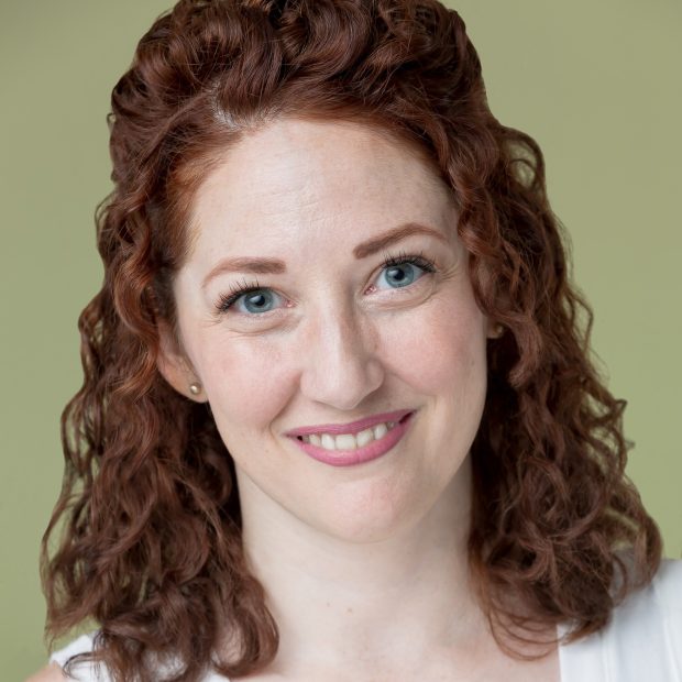 Woman with curly red hair and blue eyes in a white shirt with a green background